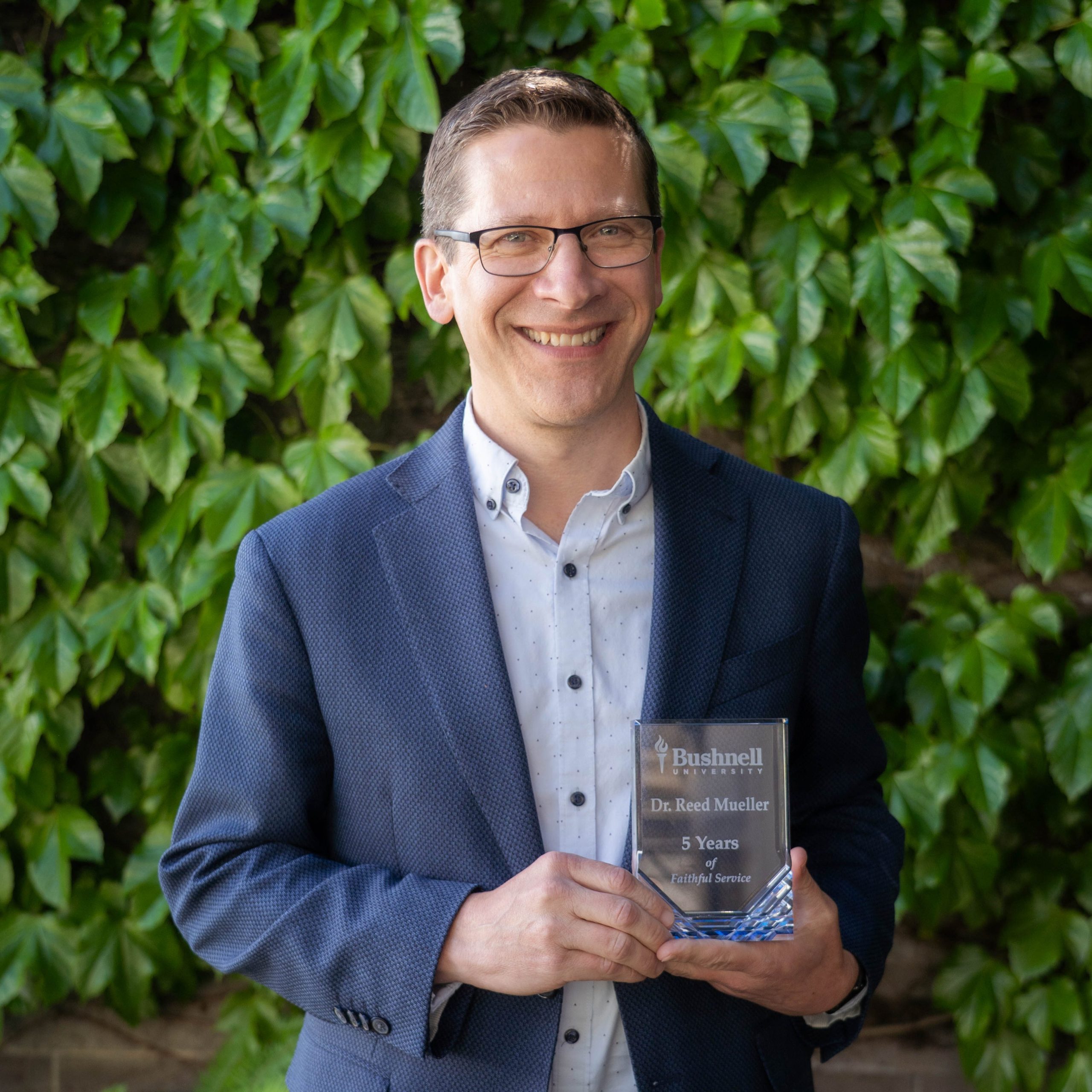 Employee recognized for 5 years of faithful service while holding a commemorative award outdoors on campus