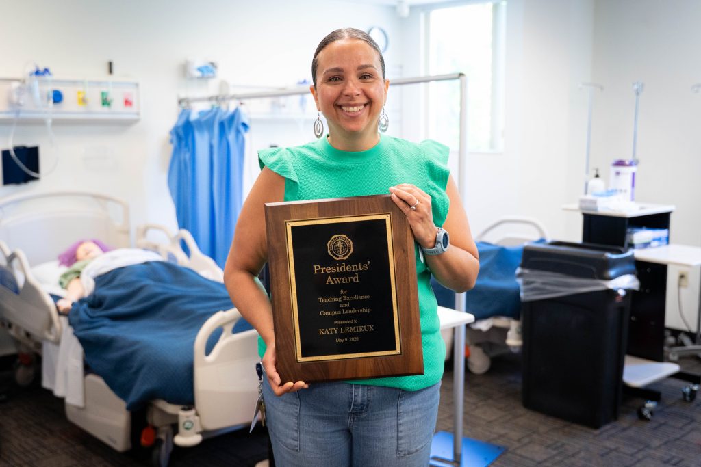 Faculty member holding a President’s Award plaque inside a nursing or healthcare simulation classroom
