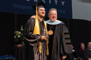 Graduate receiving an academic award while posing with the university president during commencement ceremony