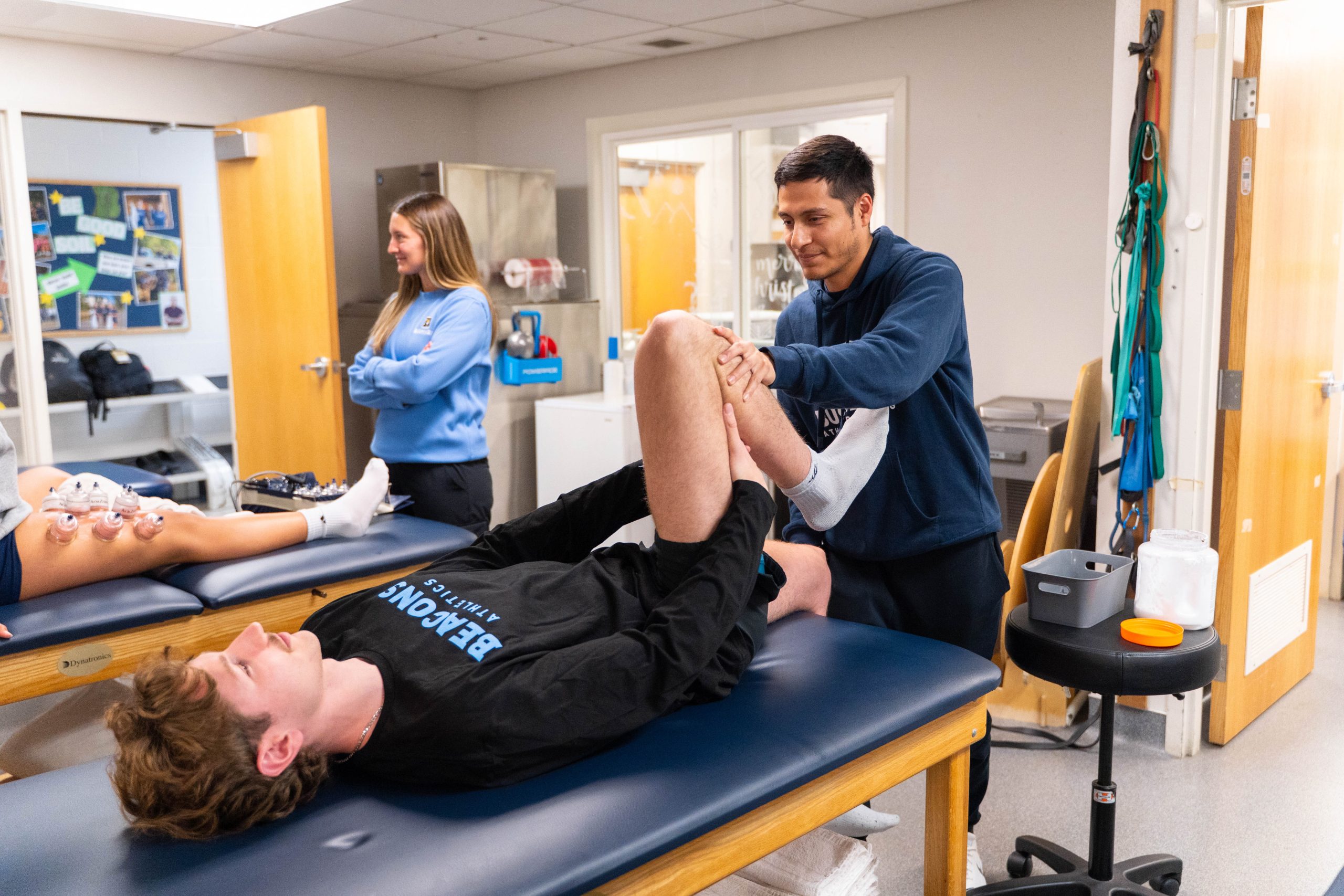 Athletic trainer aiding a student-athlete doing a leg stretch in a training facility