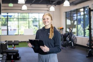 Kinesiology student standing in a gym with a clipboard for an athletic trainer internship