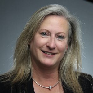 Professional headshot of a business woman with blonde hair against a grey background