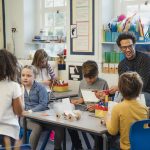 A busy elementary school classroom with students constructing models alongside a teacher