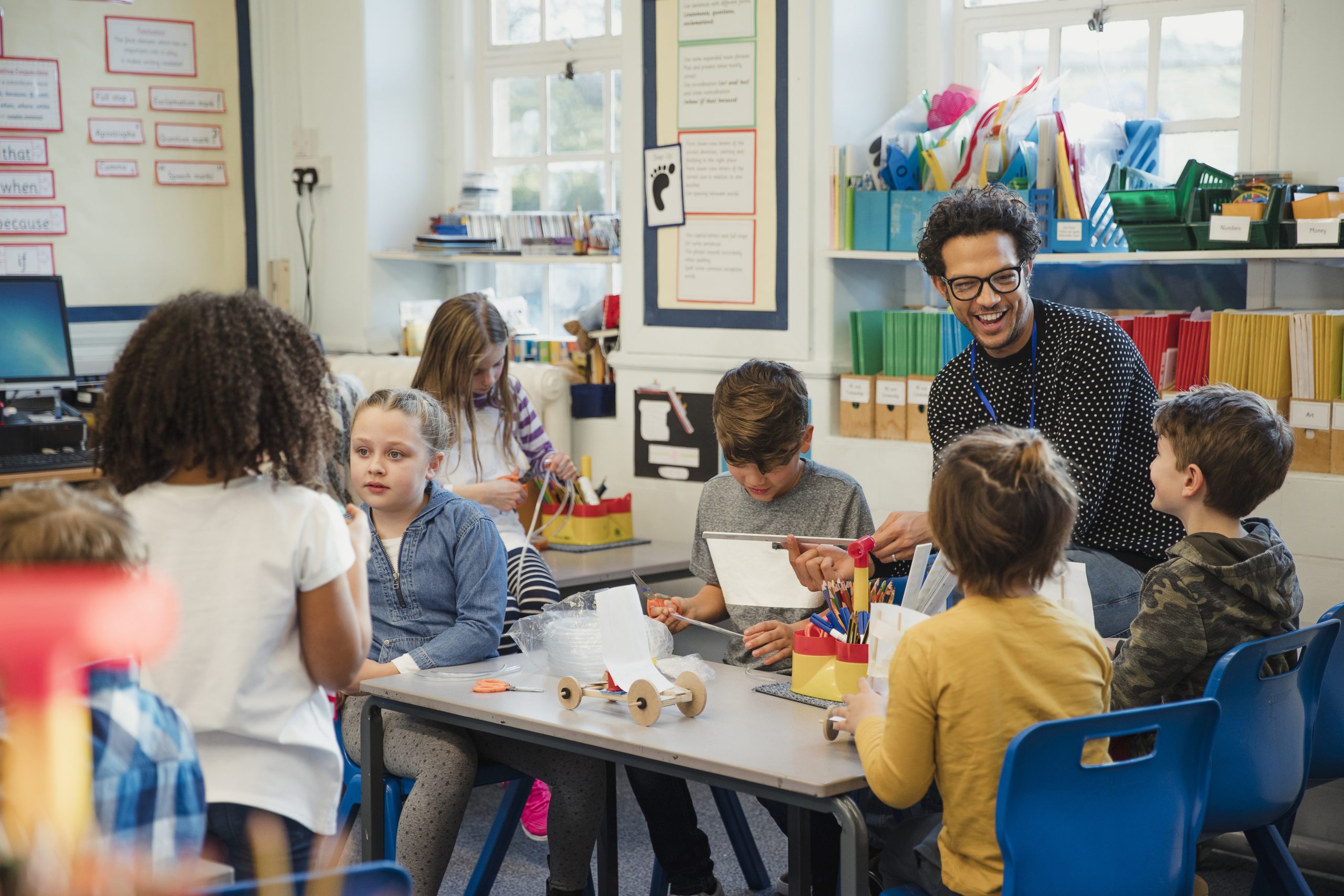 A busy elementary school classroom with students constructing models alongside a teacher