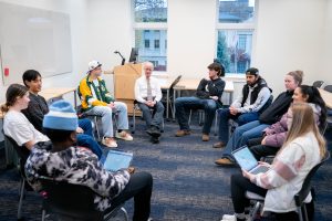 Male professor sits in circular class discussion with students