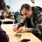 Computer science student wiring a practice circuit board in a classroom