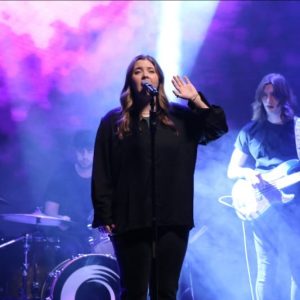 Female lead vocalist sings on high production stage with band in the background