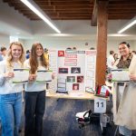 Digital marketing students holding awards beside their marketing pitch for a local business