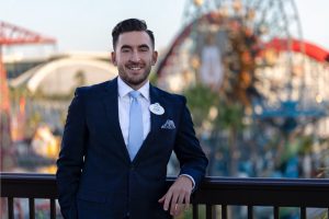 Disney hotel manager standing in front of Disneyland attractions in professional business attire