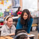 Elementary school teacher helps student on their computer during class