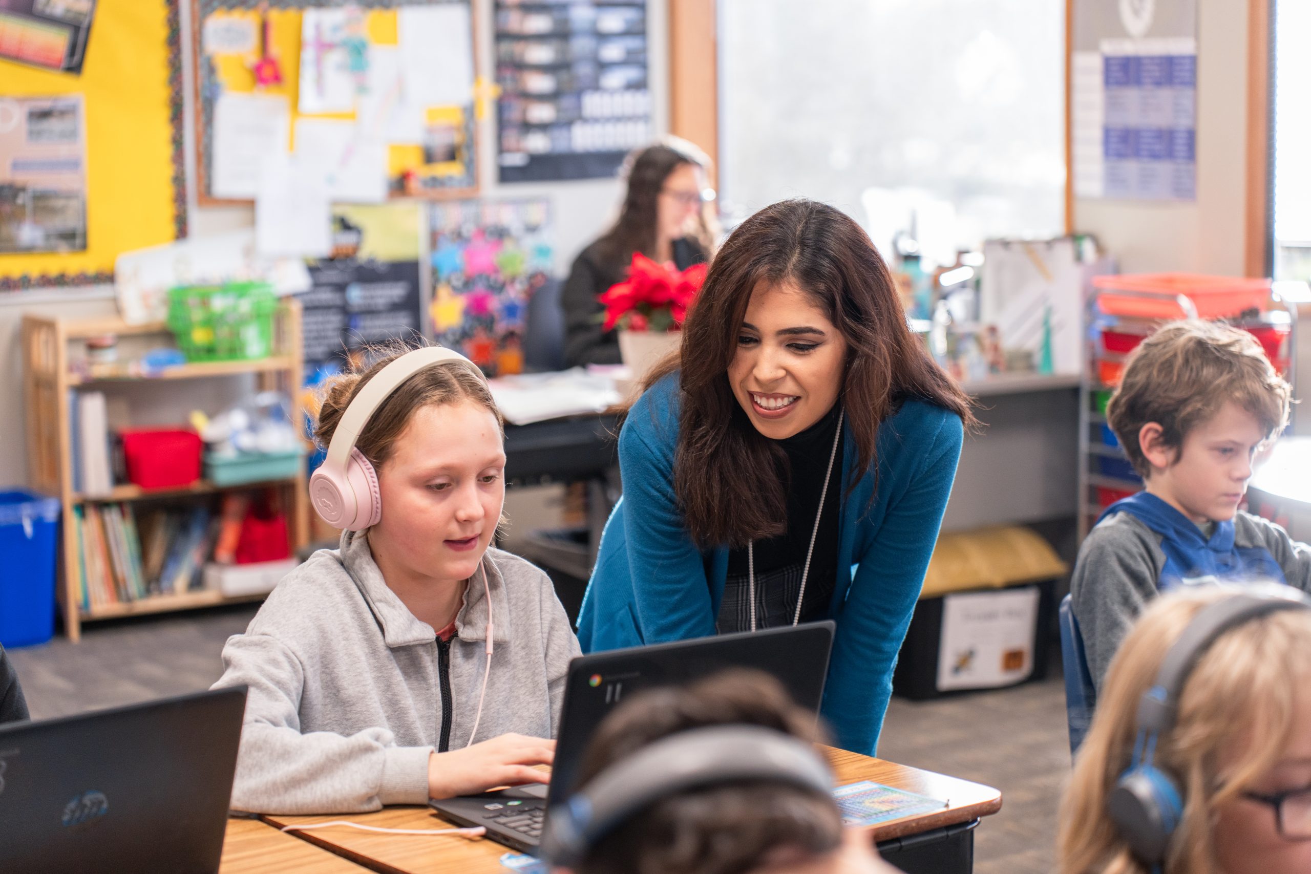 Elementary school teacher helps student on their computer during class