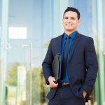 A finance professional in a suit holds a binder outside of an office building waiting for an interview