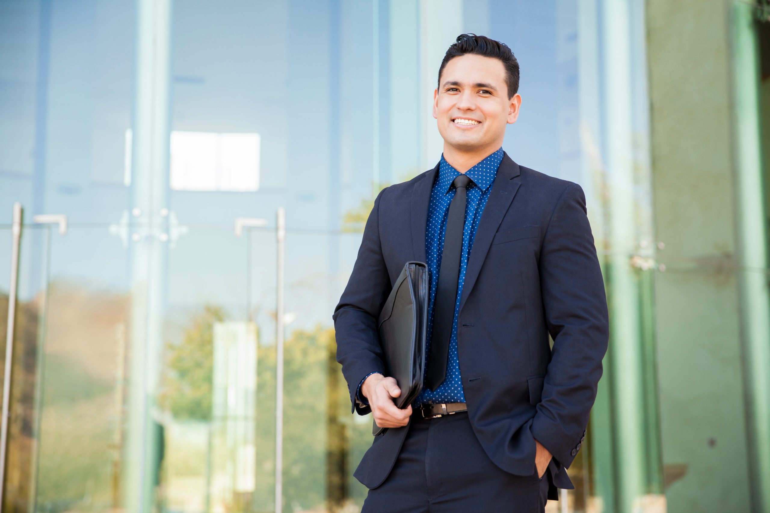 A finance professional in a suit holds a binder outside of an office building waiting for an interview