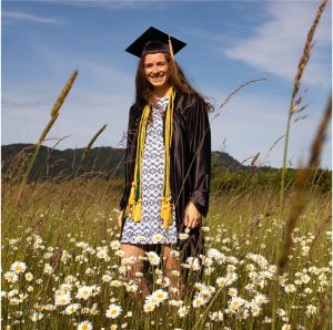 Student in graduation robes smiling in a field of flowers