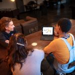 Graphic design students collaborating around a tablet displaying digital design work