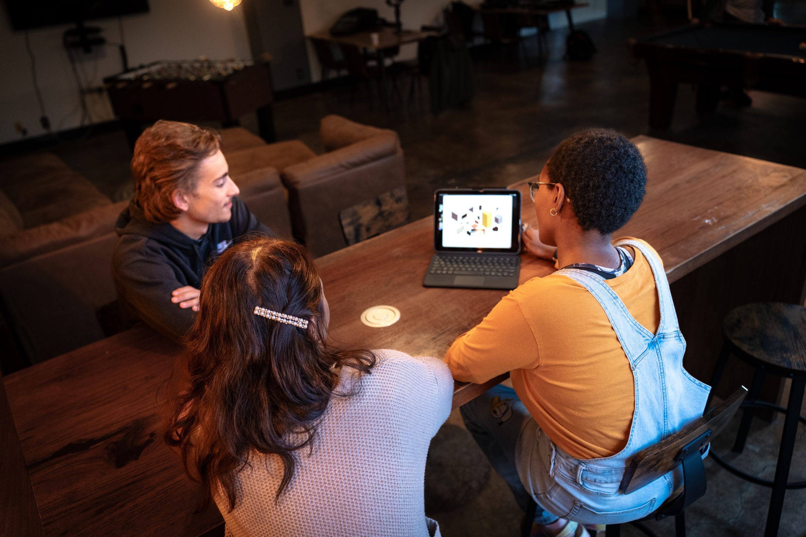 Graphic design students collaborating around a tablet displaying digital design work