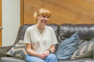 Intern wearing a cross necklace while seated on a couch during a conversation