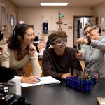 Female professor showing off a test tube with liquid to students during a lab excercise