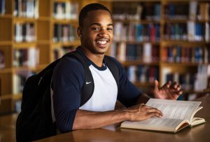English student reading a book at a table in a library setting