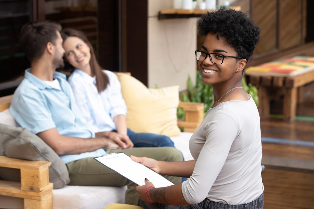 A marriage counselor with clipboard works with a smiling young couple