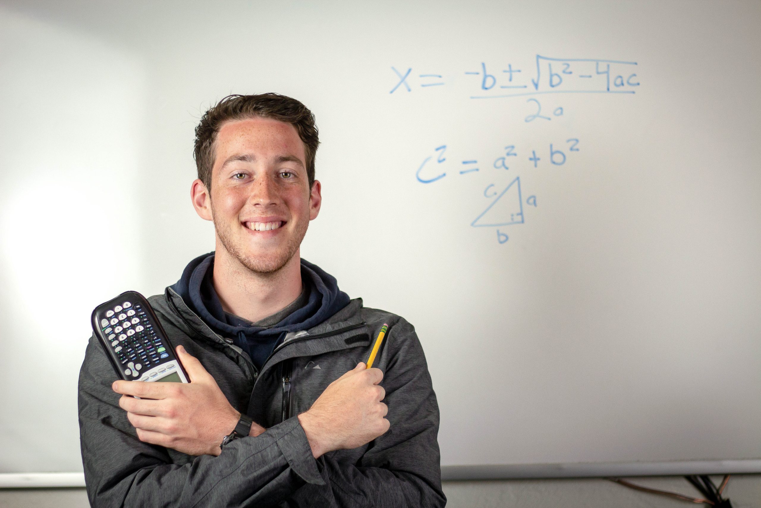 Math student tutor poses with a calculator with a mathematical equation on a whiteboard