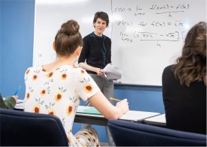 Female mathematics professor teaches lengthy equation on whiteboard to class