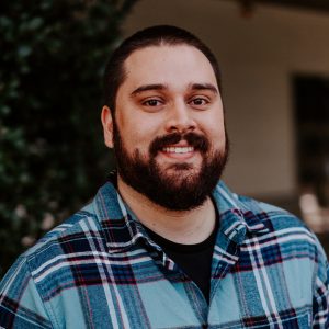 Male student with beard smiles in a blue plaid shirt