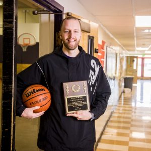 Physical education teacher receives Teacher of the Year award while holding a basketball in a school hallway