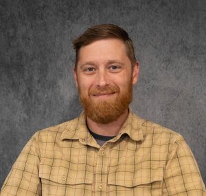 Headshot of a man in a plaid shirt against a grey background