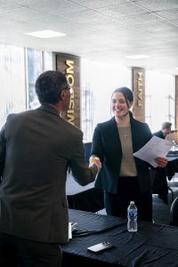 Student in professional attire shaking hands with an employer during a networking event
