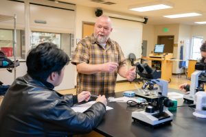 Male professor helps student with microscope in biology lab