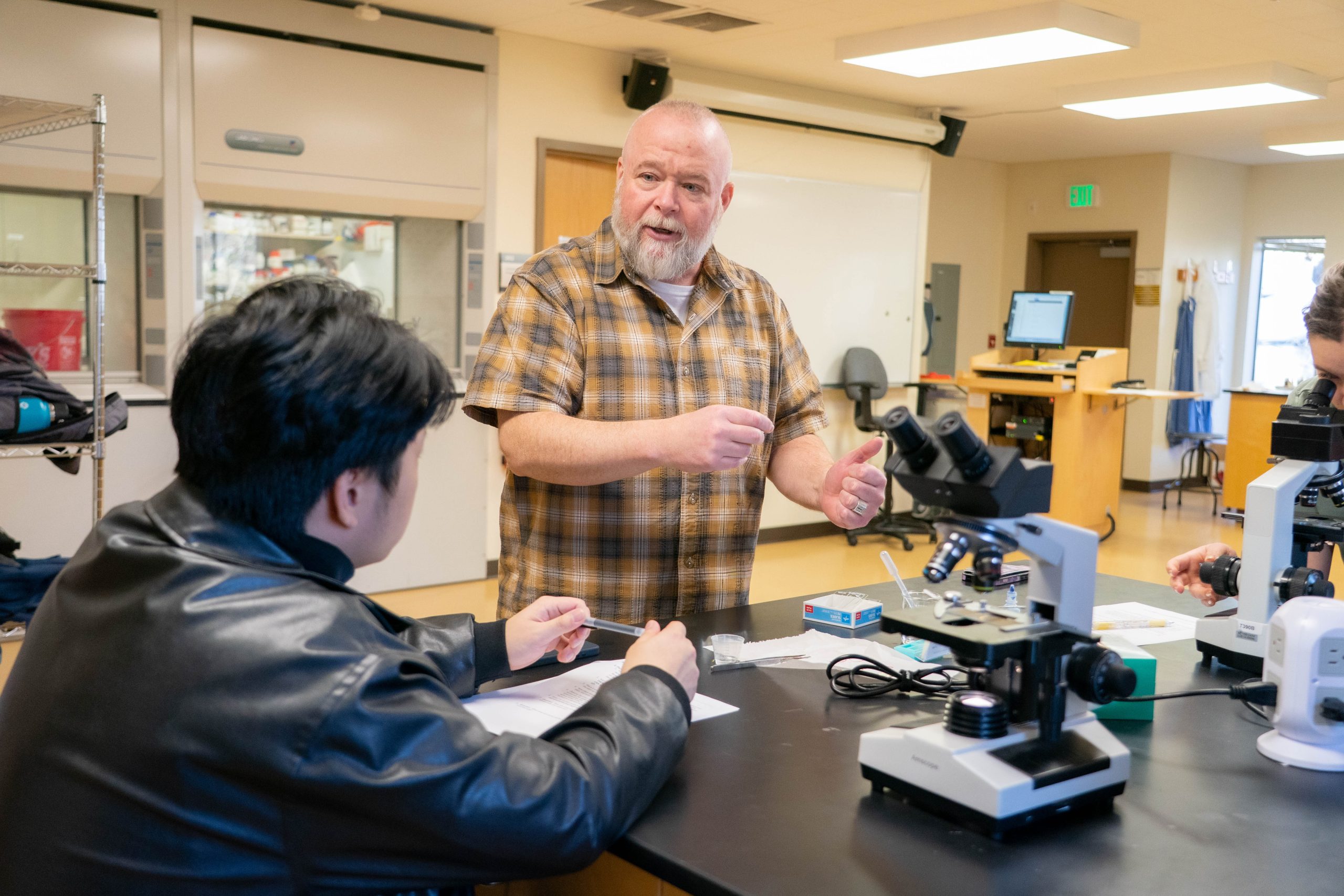 Male professor helps student with microscope in biology lab