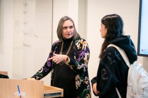 Female professor speaks to an English student at the front of a classroom