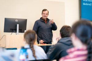 Male professor standing at the front of class selecting a student with their hand raised