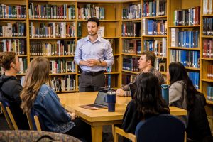 Business professor speaks to students around a table in a library