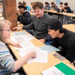 professor assisting students on finance worksheets in class