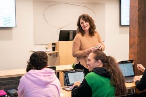 A female psychology professor giving an assignment within a classroom to students on computers