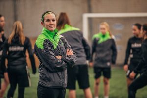A confident recreational soccer coach poses with team players in the background