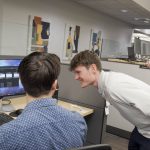 Student interns working together at computer monitors in an office setting