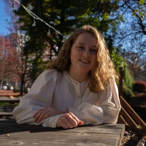 Female student sits at picnic table outside in the sun