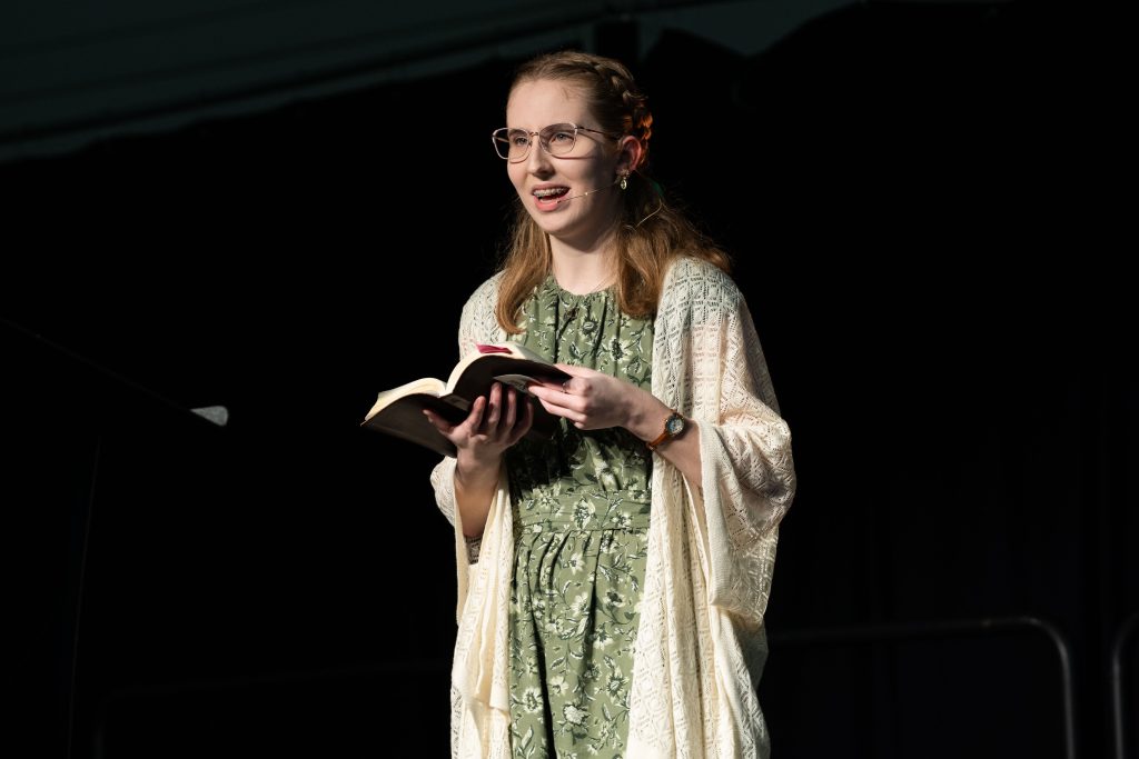 Young female student preaches on stage while holding a bible