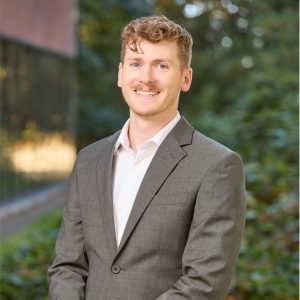 Professional headshot of a student in a gray suit outdoors
