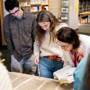 Students read a Torah scroll alongside their theology professor in a library