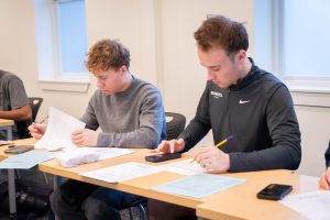 Accounting students calculating expenses on classroom worksheets with calculators