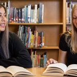 Two students reading books at the same table in the campus library