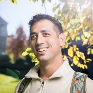 Headshot of a male student with black hair and backpack in the sun