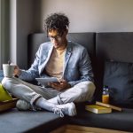 A young man studying with a digital tablet and books while sitting on a couch