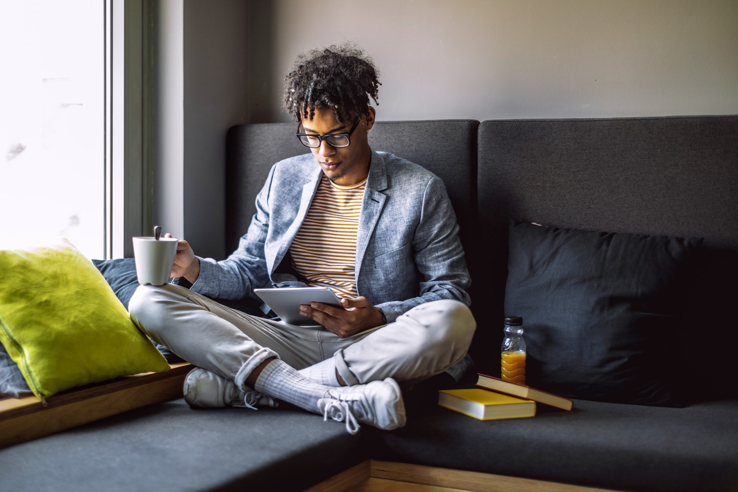 A young man studying with a digital tablet and books while sitting on a couch