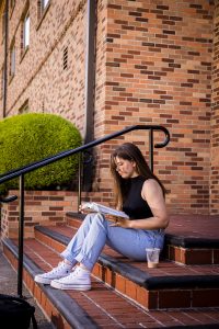 Bushnell University student sits on campus steps reading a textbook and studying outdoors near a brick academic building.