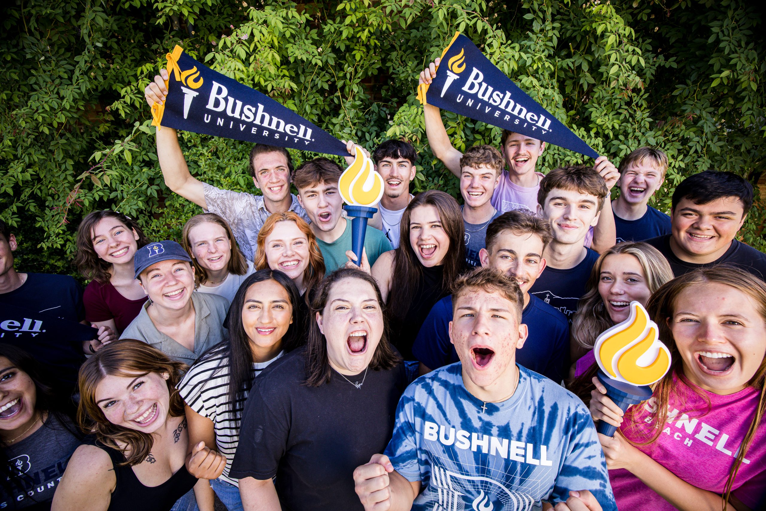 Bushnell University students gather together holding school pennants and torch props while celebrating campus community and school spirit.
